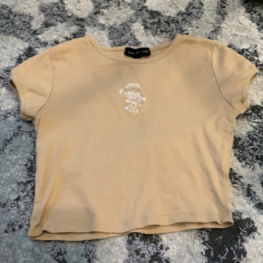 Tan colored shirt that has a flower on it